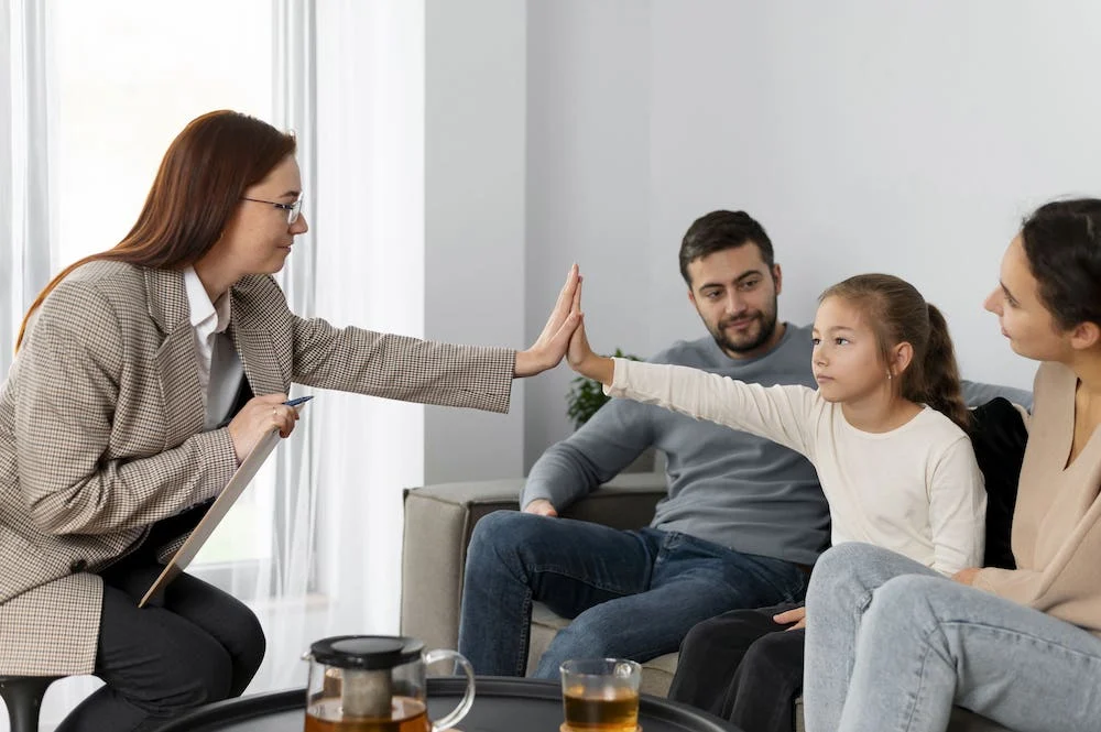 Picture Showing Family in Therapy - young girl high-fiving her therapist